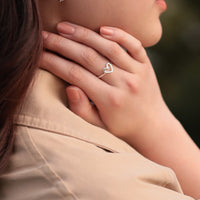 Close up of a womans hand wearing a silver open heart shaped ring with a blurred background