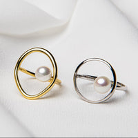 A gold and a silver rings on a white background. Both circular in design and featuring a white pearl in the centre,.