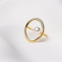 A ring with a gold vermeil band and a silver circular frame containing a pearl, placed on a white fabric surface.