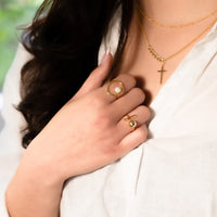 A model wearing a gold circular designed ring featuring a pearl in the centre.