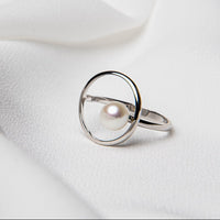 A circular shaped ring with a pearl in the centre on a white cloth background