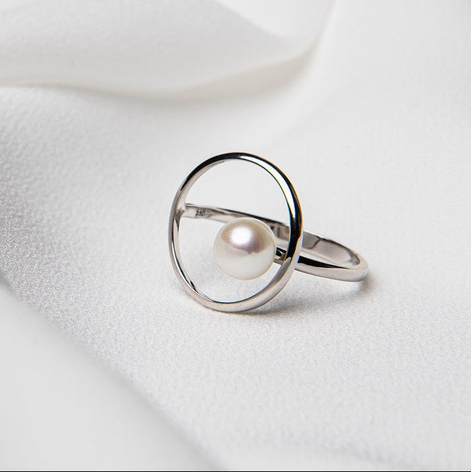 A circular shaped ring with a pearl in the centre on a white cloth background