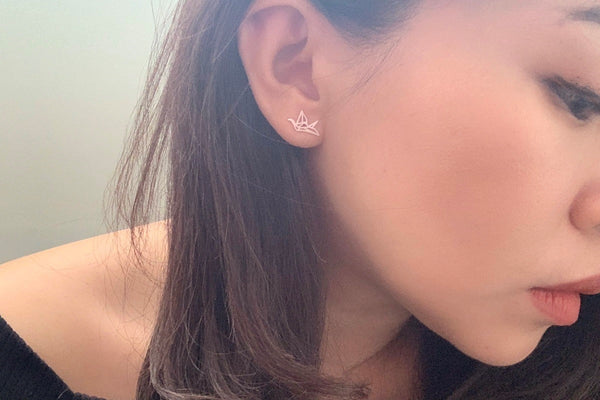 A pair of silver stud earrings designed in a origami crane shape, on a woman model.