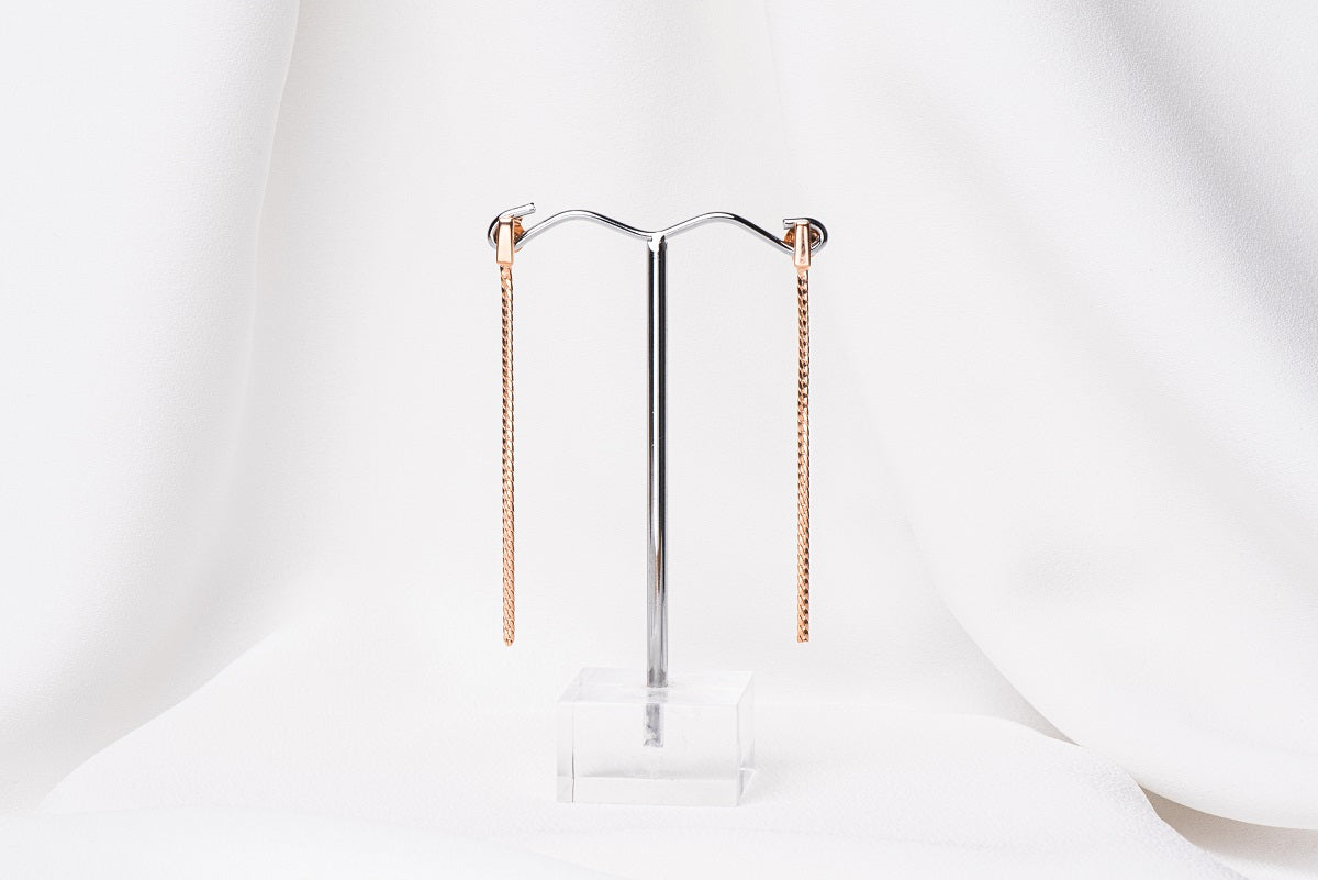 A pair of dangle earrings with butterfly back closures, crafted from sterling silver with rose gold vermeil coating, displayed on a white stand.