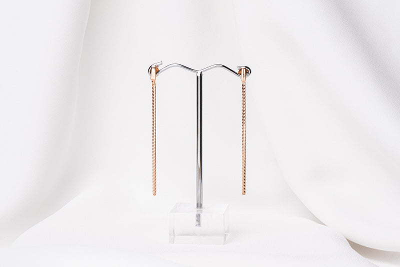 A pair of dangle earrings with butterfly back closures, crafted from sterling silver with rose gold vermeil coating, displayed on a white stand.