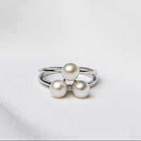 An adjustable size ring with a polished finish, featuring a silver band and three round white pearls on top, placed on a white fabric surface.