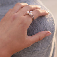Close up of a womans hand wearing a sterling silver ring featuring three white pearls.