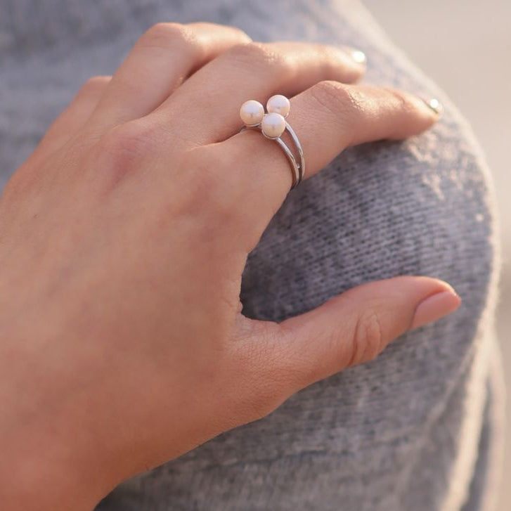 Close up of a womans hand wearing a sterling silver ring featuring three white pearls.