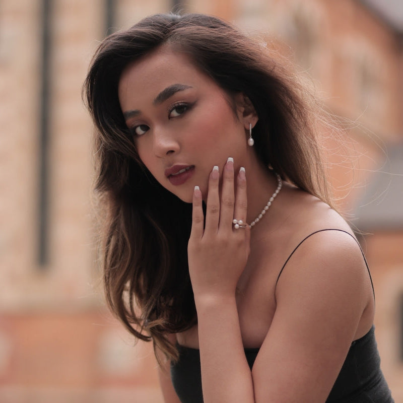 A model wearing a silver ring featuring three white pearls with a blurred city background.