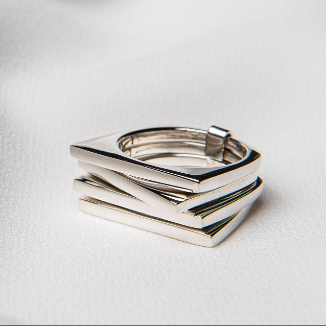 A polished silver ring with a geometric, rectangular design, displayed on a white fabric surface.