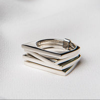 A polished silver ring with a geometric, rectangular design, displayed on a white fabric surface.