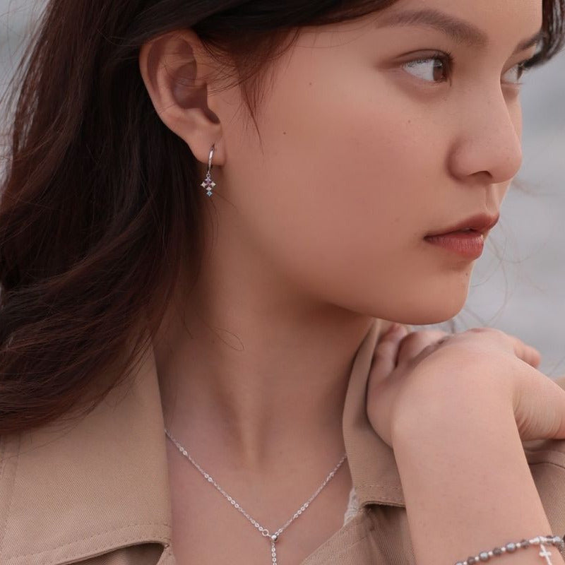 A women wearing a pair of sterling silver hoop cross earrings with a multicolored dangle design.
