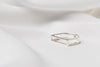 A polished silver ring with a rectangular shape on a white fabric surface.