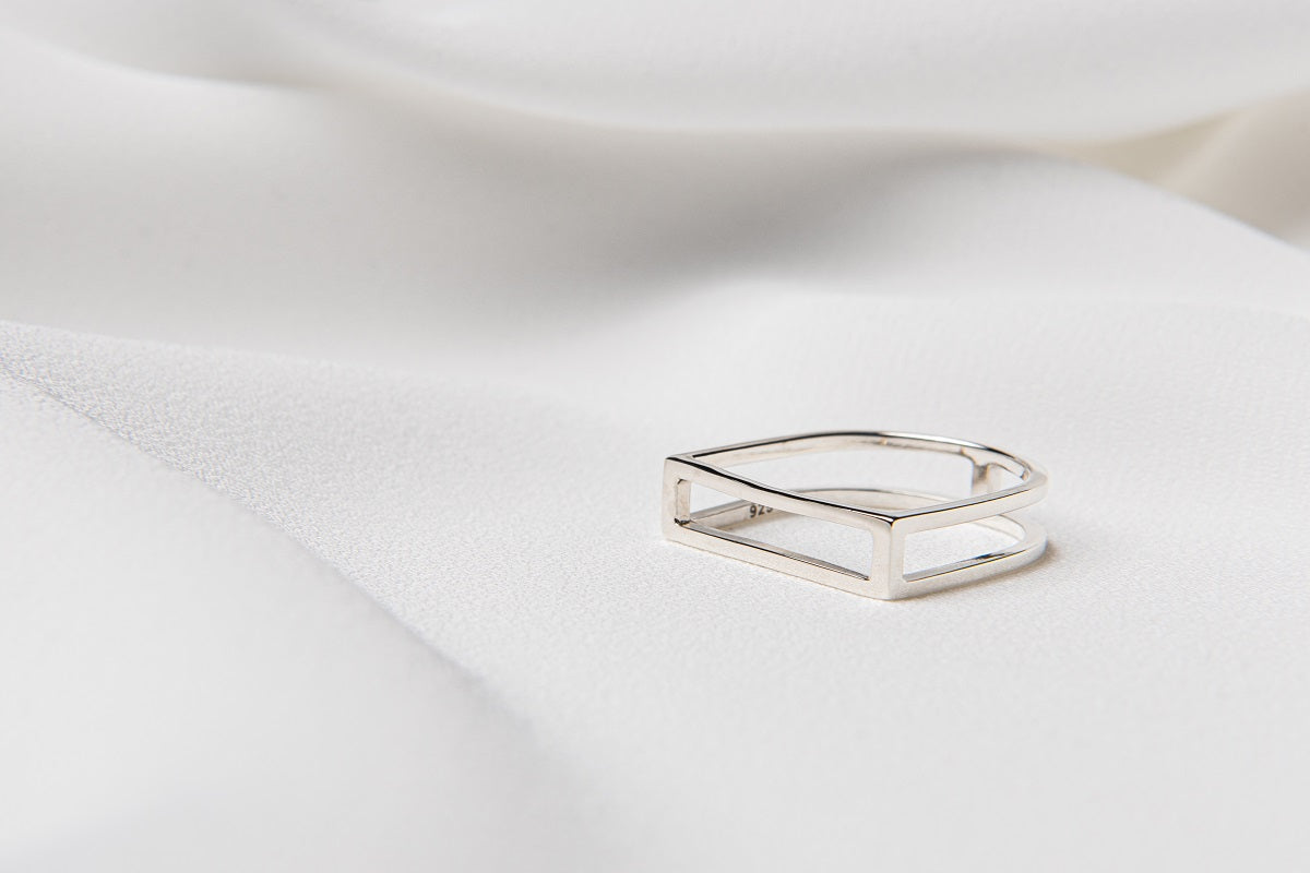 A polished silver ring with a rectangular shape on a white fabric surface.