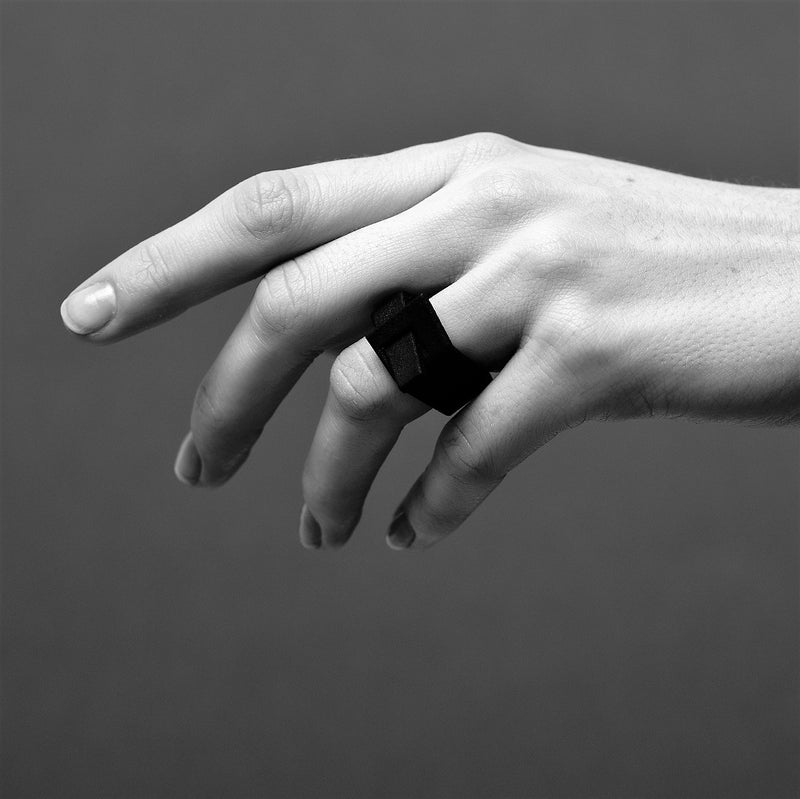 Black and white close up of a hand wearing a matt black ring