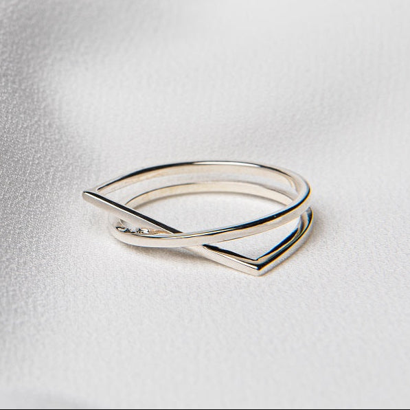 A polished silver ring with a simple, elegant design, displayed on a white fabric surface.