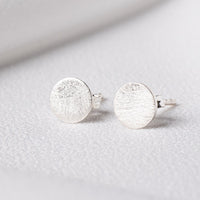 Pair of brushed sterling silver round studs on a white cloth background
