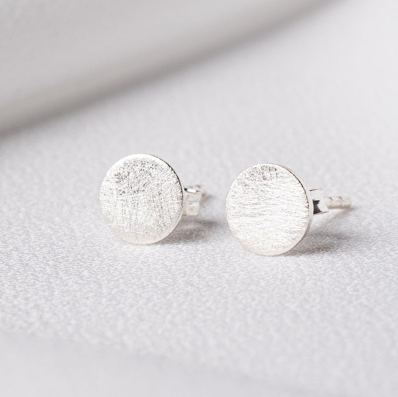 Pair of brushed sterling silver round studs on a white cloth background