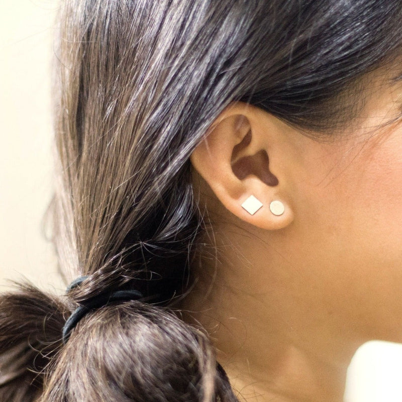Close up of a model wearing Sterling silver studs, one square and one round.