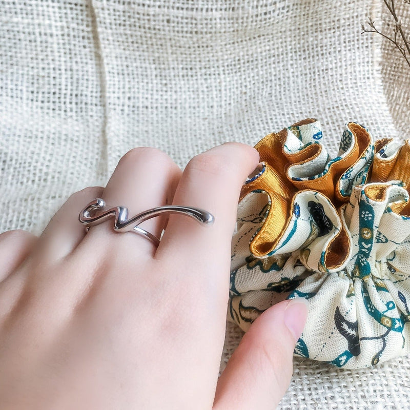 A close up picture of a womans hand wearing a polished silver ring in the shape of a scribble.