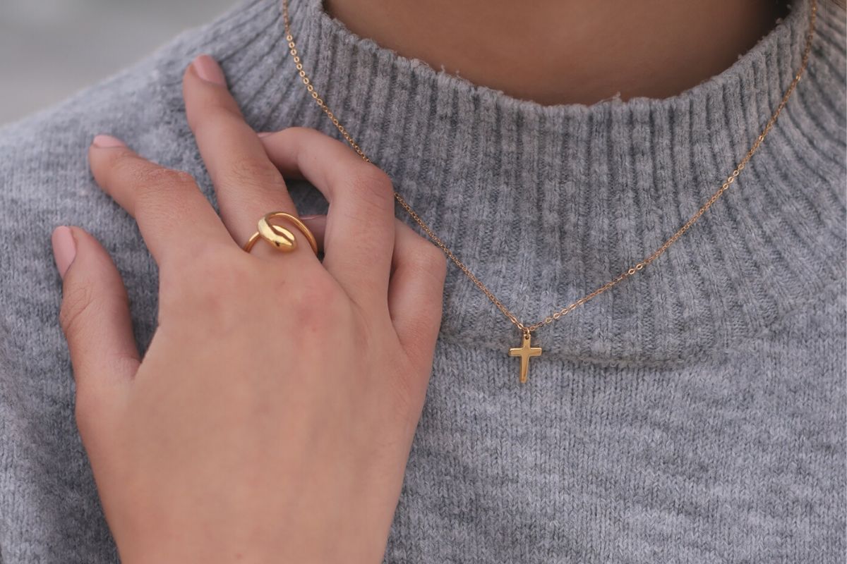 A gold chain necklace with a small gold cross pendant worn by a woman