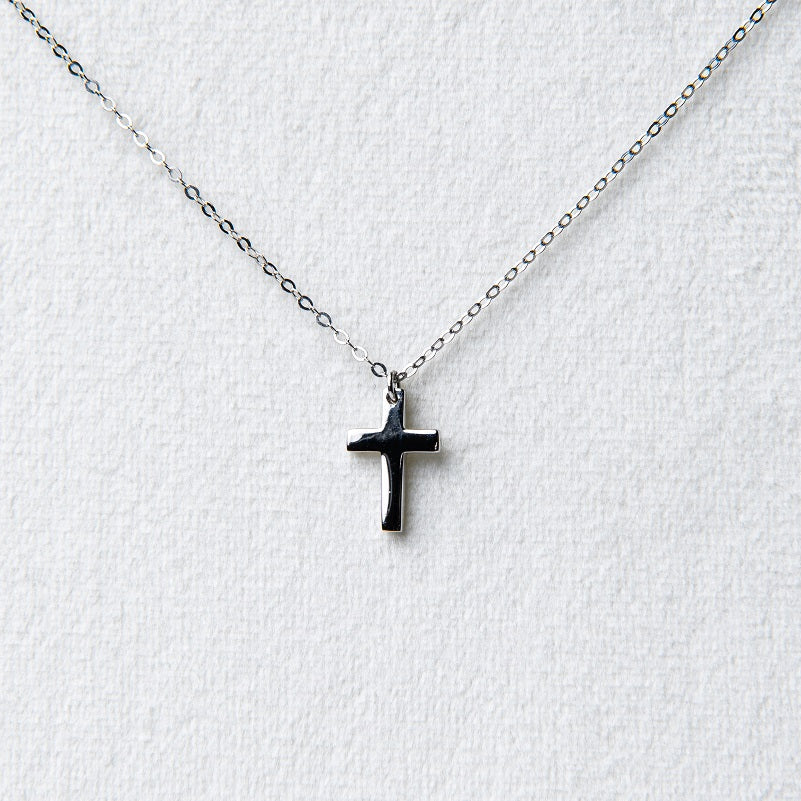 A simple silver cross pendant on a fine silver chain displayed on a white jewellery display seting.