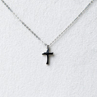 A simple silver cross pendant on a fine silver chain displayed on a white jewellery display seting.