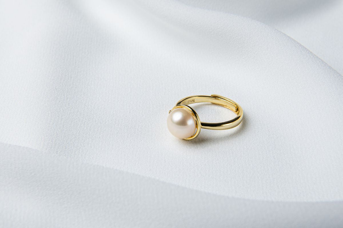 A gold pearl ring on a white cloth background