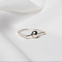 A polished silver ring with a ball centerpiece, placed on a white silky fabric surface.
