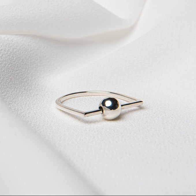 A polished silver ring with a ball centerpiece, placed on a white silky fabric surface.