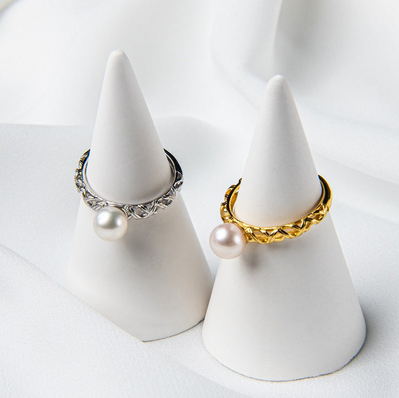 A gold and a silver ring, both featuring a single white pearl, both on a white display cone.