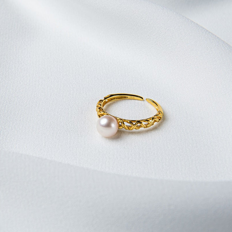 An elegant silver ring with a gold vermeil band and a single round white pearl on a silky white background.