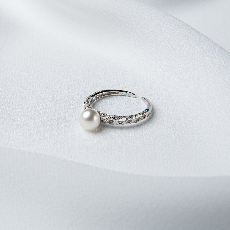 An elegant silver ring with a single round white pearl on a silky white background.