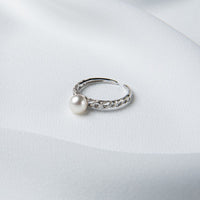 An elegant silver ring with a single round white pearl on a silky white background.