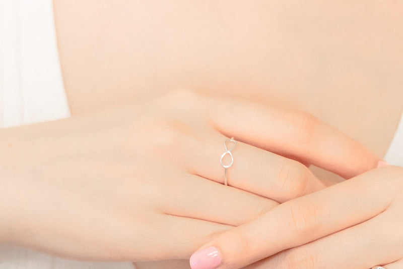 Close up of a womans hand wearing a thin silver ring in the shape of the infinity symbol