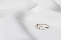 A polished silver ring with a simple design placed on a white fabric surface.