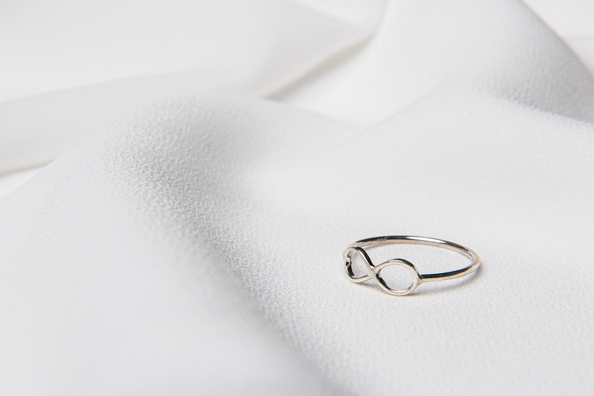 A polished silver ring with a simple design placed on a white fabric surface.