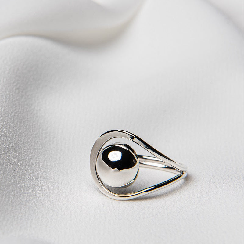 A polished silver ring with a smooth, curved design, displayed on a white silky surface.