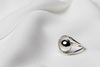 A polished silver ring with a smooth, curved design, displayed on a white silky surface.