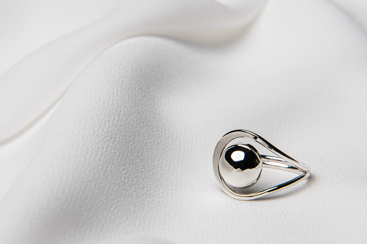 A polished silver ring with a smooth, curved design, displayed on a white silky surface.