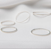 A collection of polished silver rings displayed on a white fabric surface.
