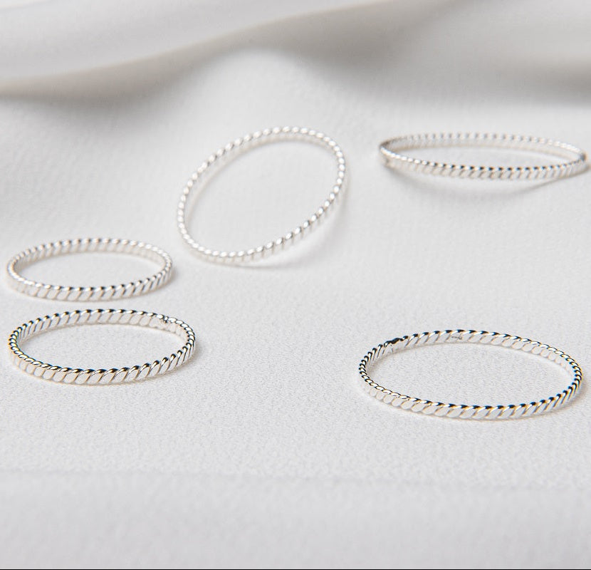 A collection of polished silver rings displayed on a white fabric surface.