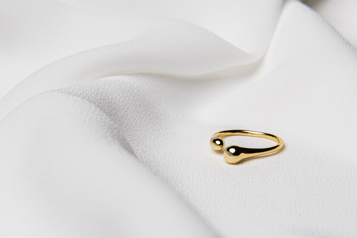 A polished, gold ring with a simple design, displayed on a white fabric surface.