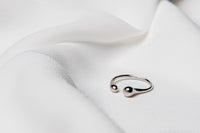 A polished, silver-colored ring with a simple design, displayed on a white fabric surface.