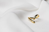 A polished gold ring with a simple elegant design, displayed on a white fabric background.