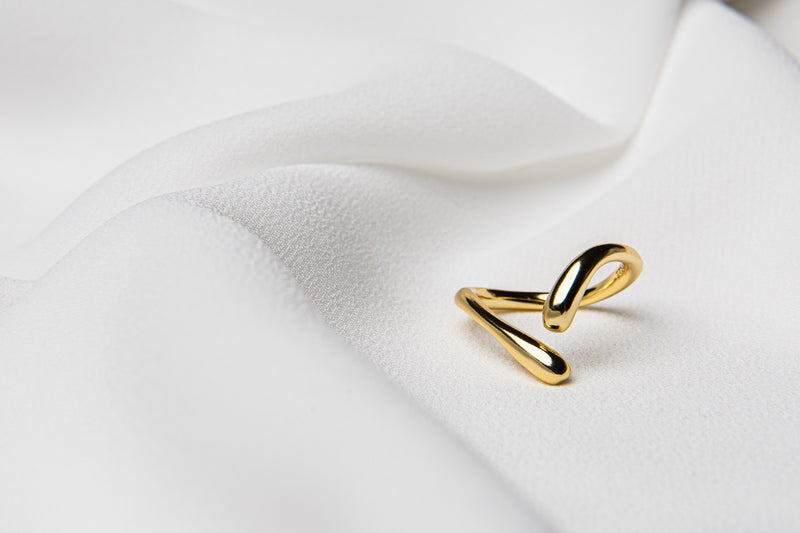 A polished gold ring with a simple elegant design, displayed on a white fabric background.