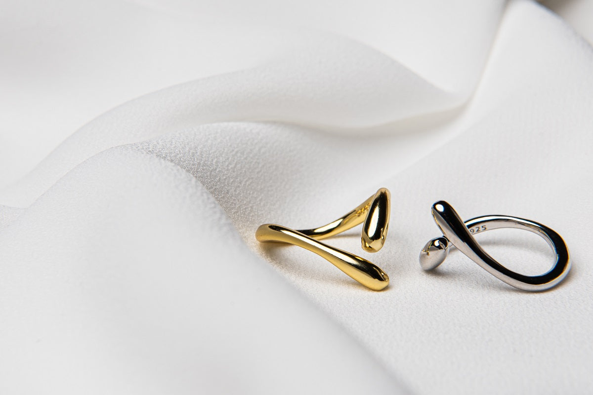 A polished gold ring and a polished silver ring with a simple elegant design, displayed on a white fabric background.