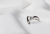 A polished silver ring with a simple elegant design, displayed on a white fabric background.