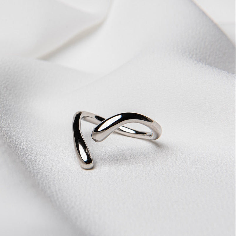A polished silver ring with a simple elegant design, displayed on a white fabric background.
