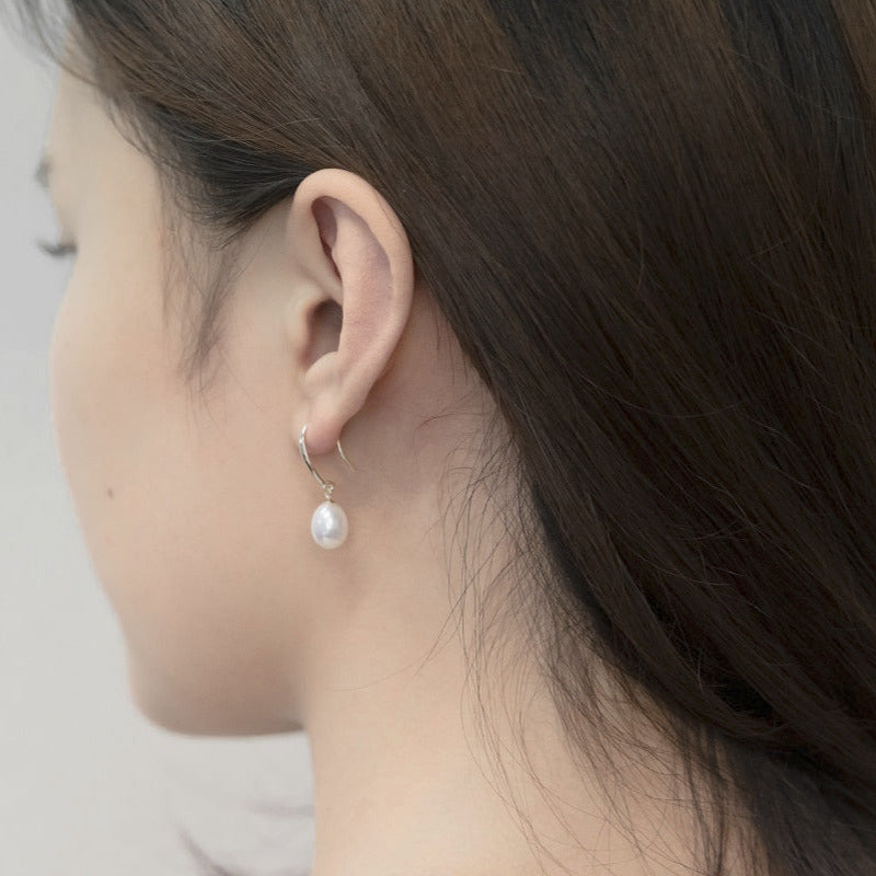 A pair of dangle pearl hook earrings in silver, worn by a woman model